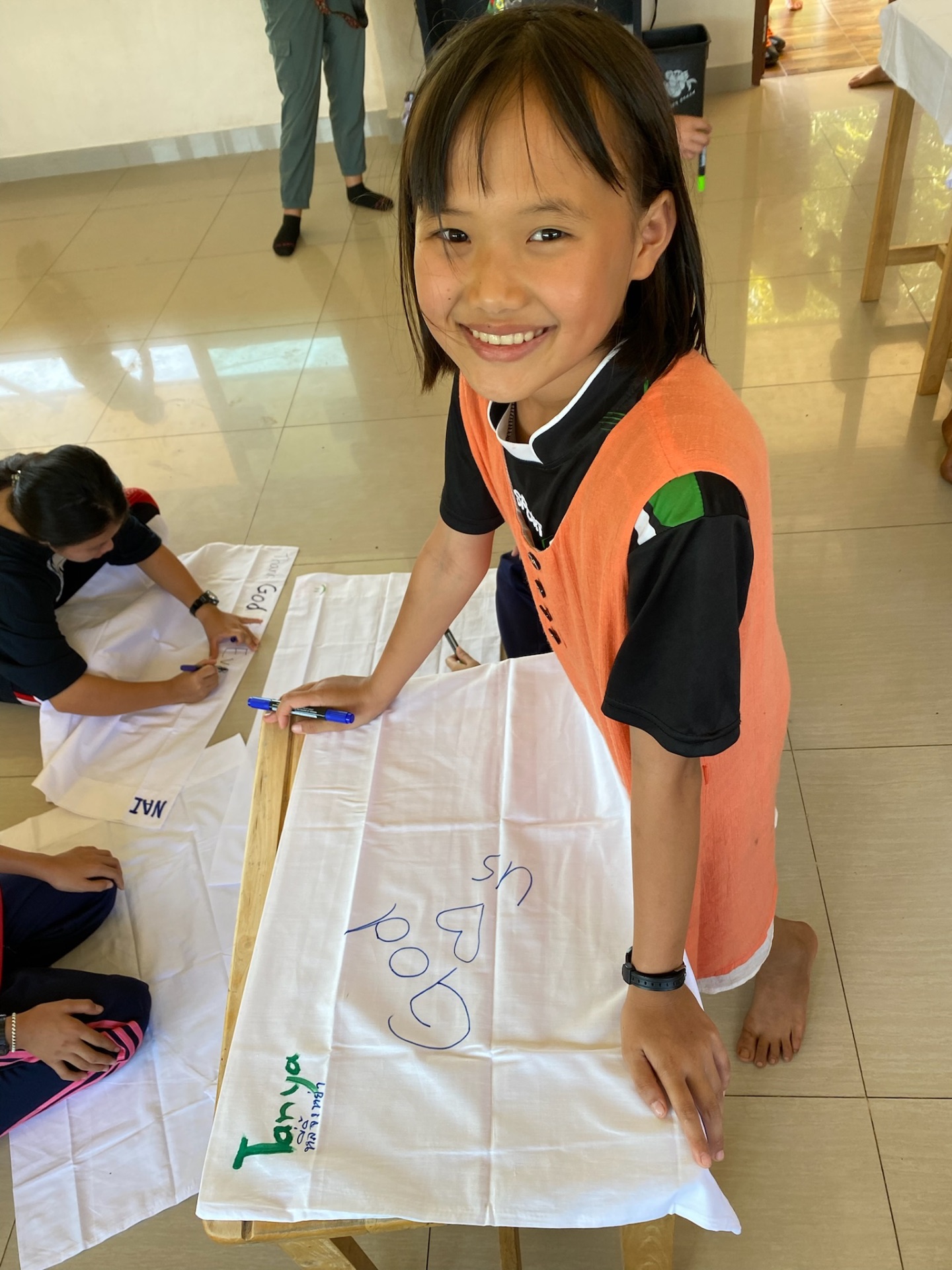 Student writing 'God loves us' on a banner at the Village of Hope