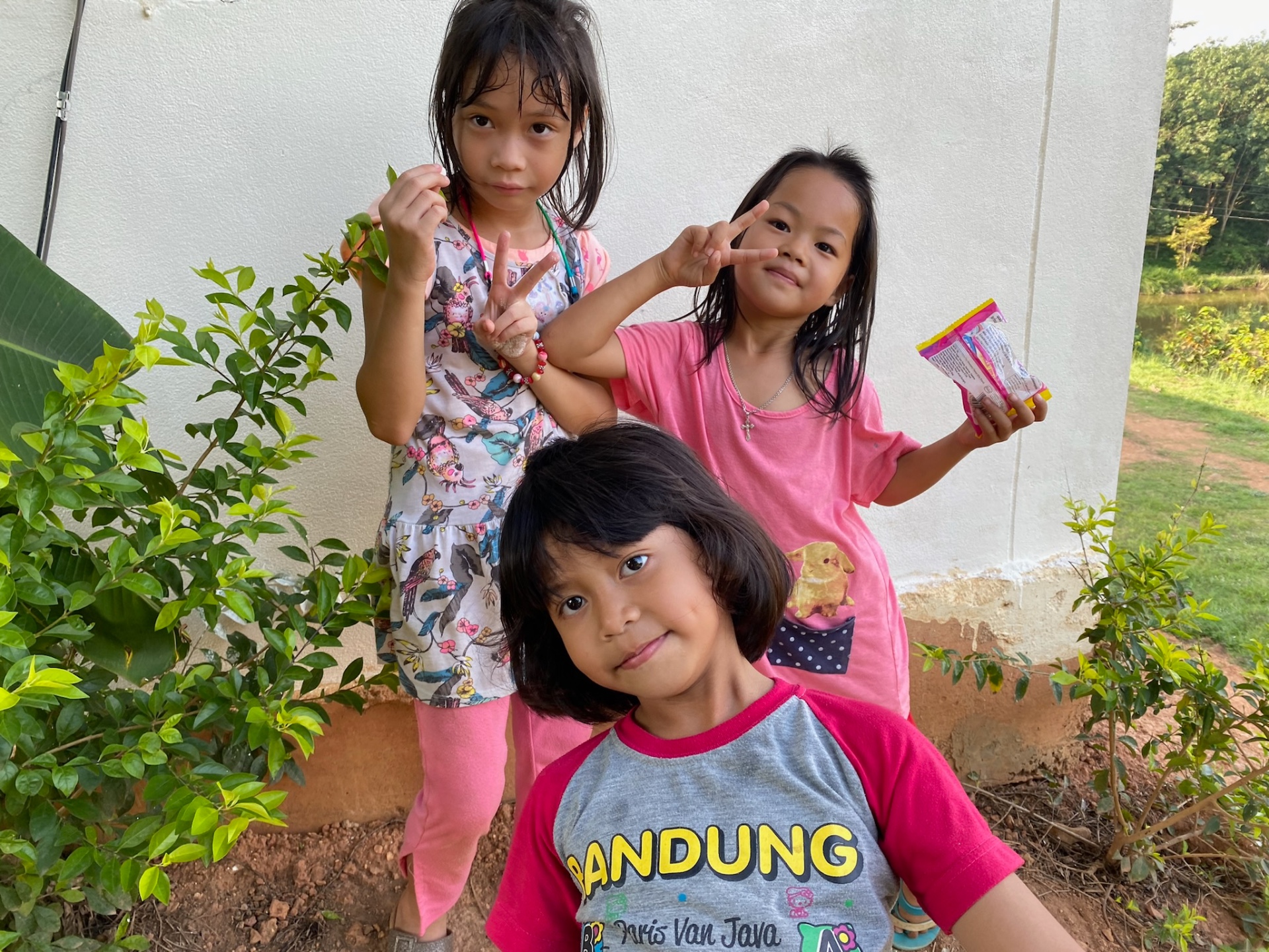 Three children making peace signs by the school wall