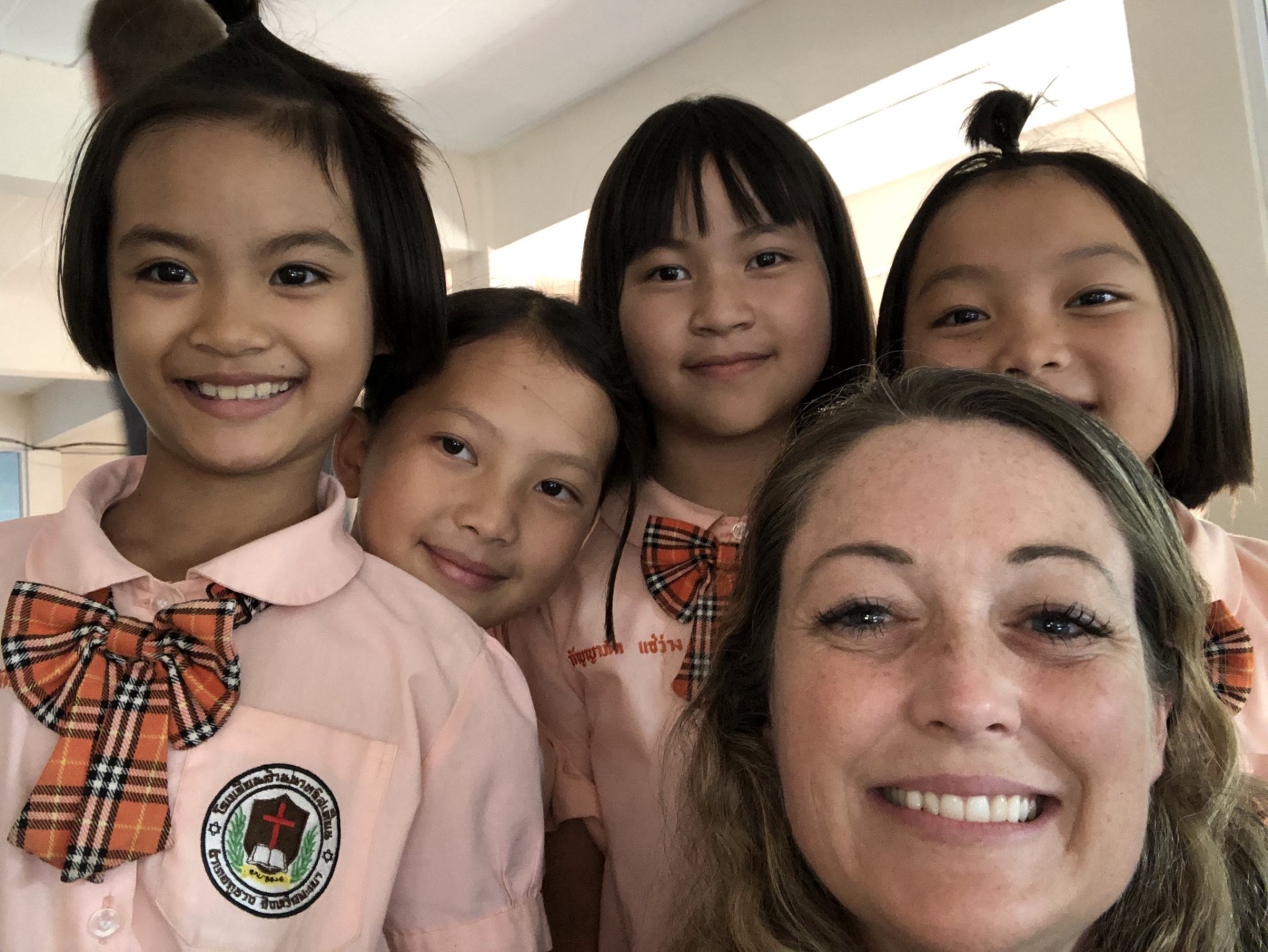 Four Lanna Christian School girls in pink uniforms with a team member, smiling for a selfie