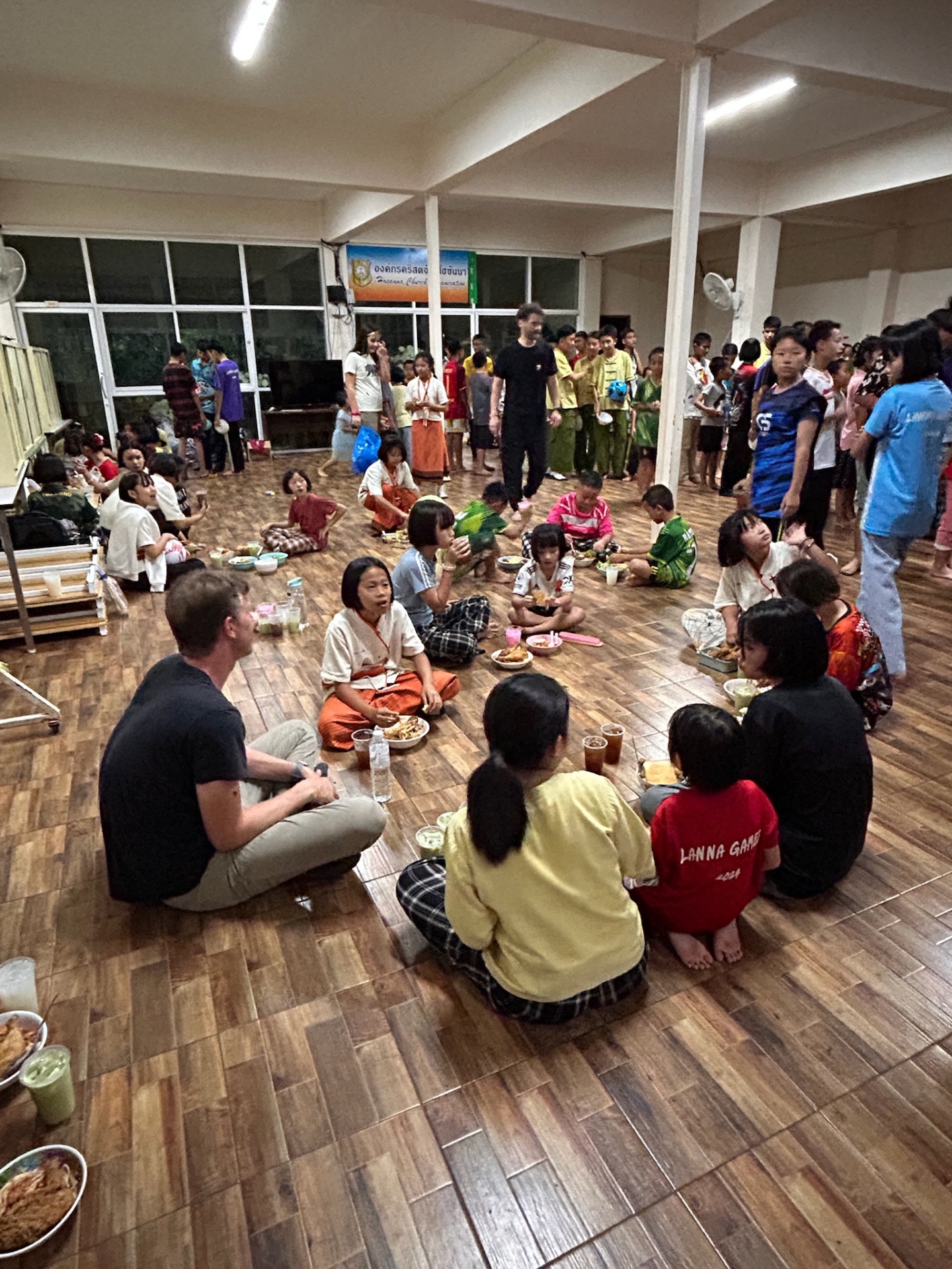 Children and team eating dinner together on the floor of the dining hall