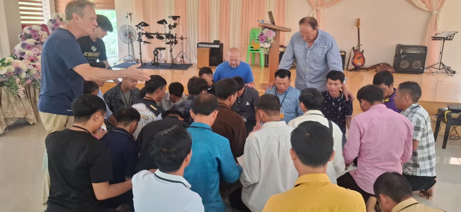 Circle of Laotian pastors kneeling in prayer at the front of the sanctuary