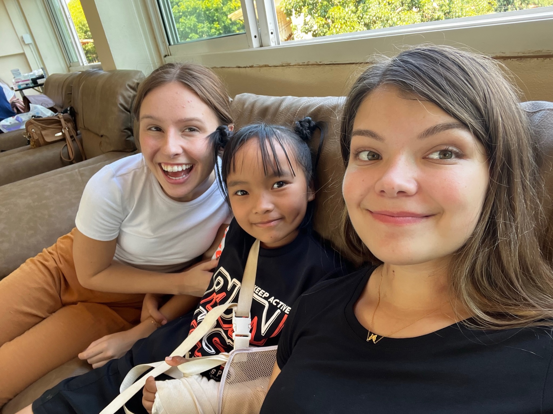 Two teen team members on a couch with a small Thai girl in pigtails between them