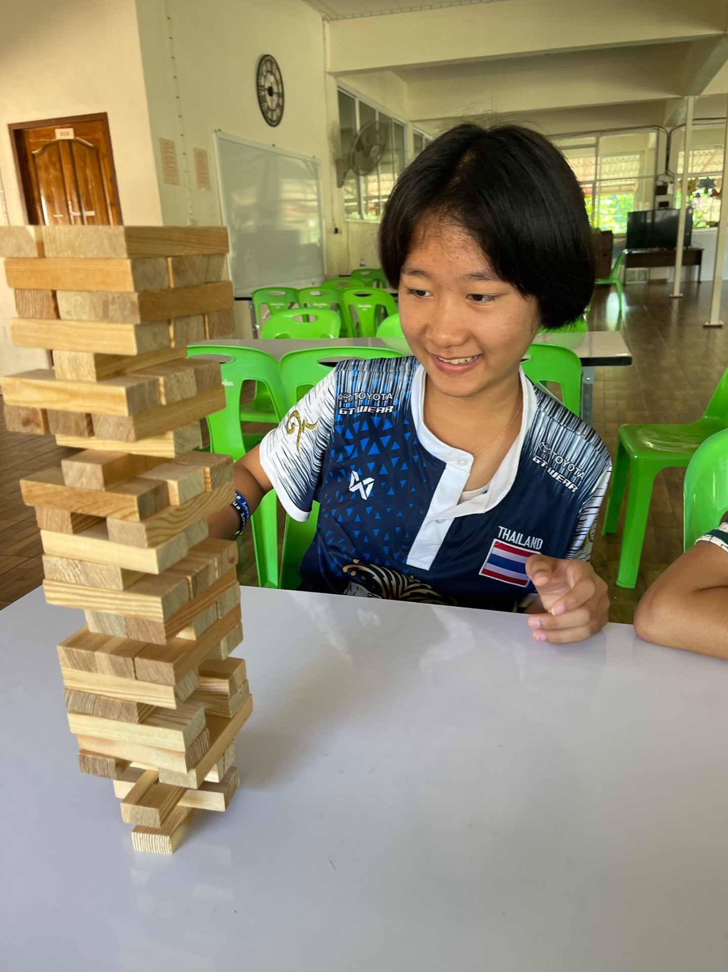 Teen girl in a Thailand jersey concentrating on a tall Jenga tower