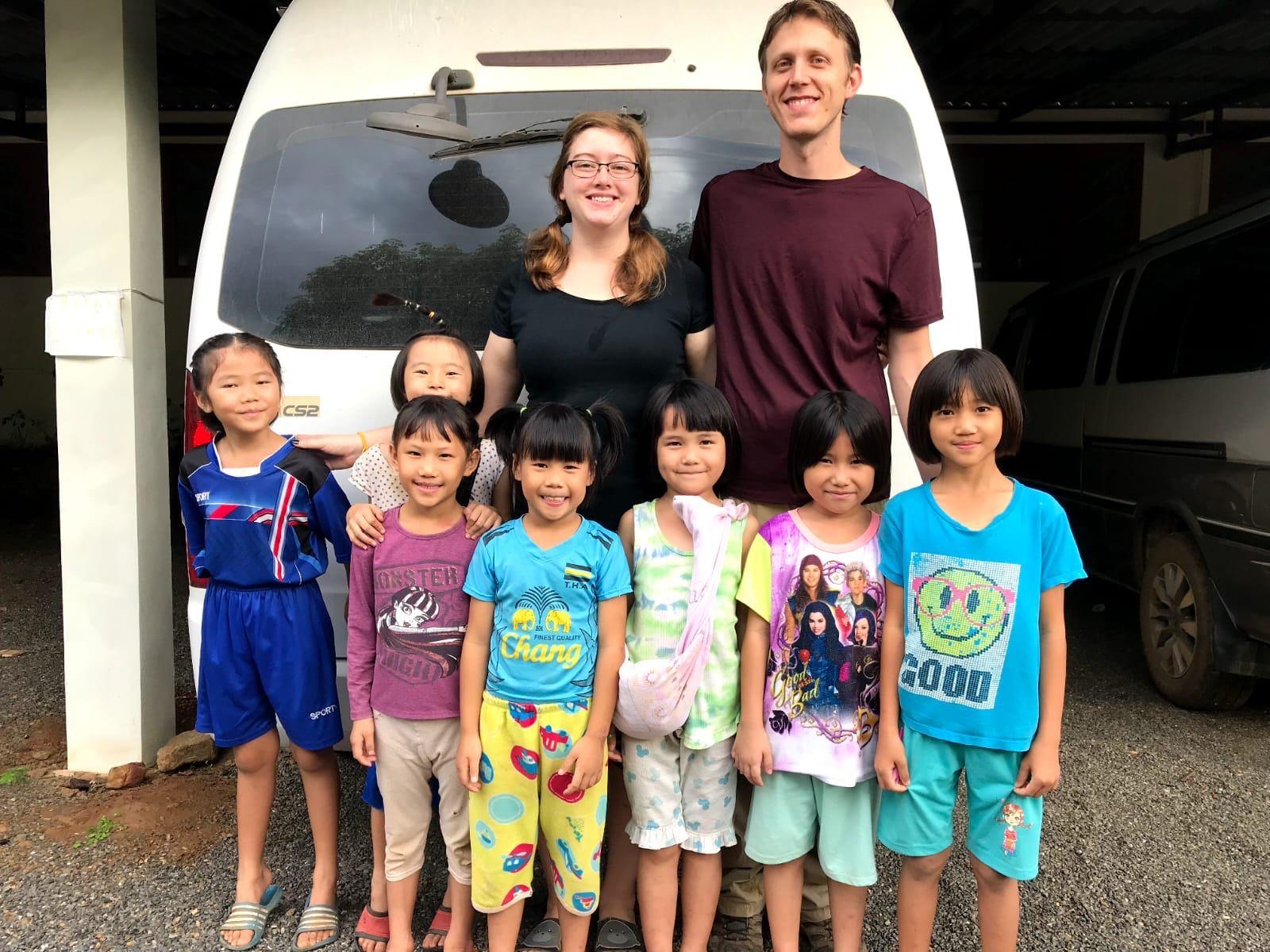 Two team members standing with a group of younger Lanna kids by the school van